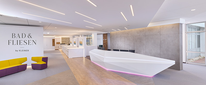 Moderne Showroom-Rezeption mit weißem Tresen, gelb-violetten Sitzbereichen und Bad & Fliesen Ausstellung