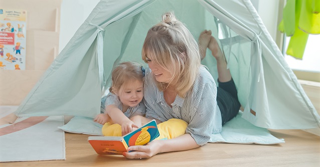 Eine Frau liest ein Buch und spielt mit einem kleinen Mädchen