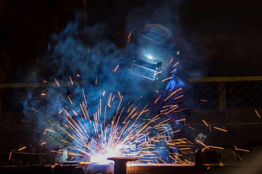 Schweißer mit Schutzmaske und Ausrüstung beim Schweißen von Metall mit Funkenflug