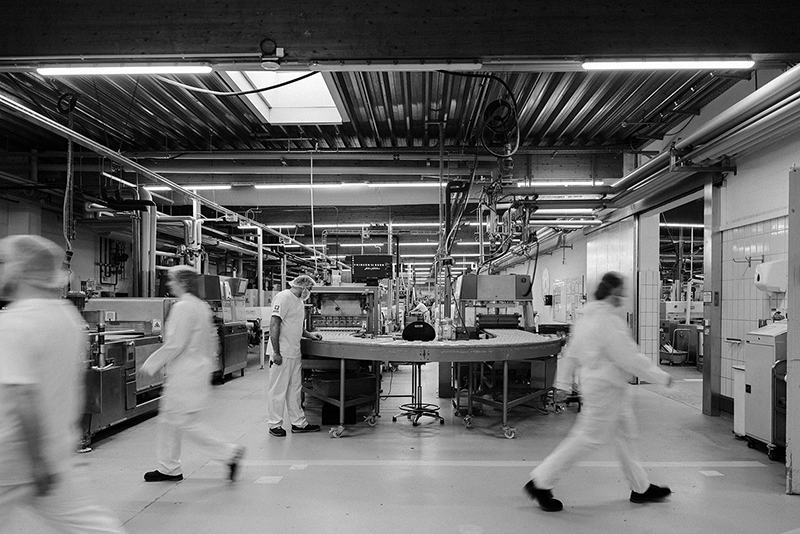 Produktionshalle mit Fließband und Mitarbeitern in Schutzkleidung