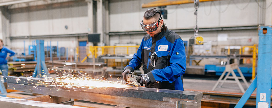 Mitarbeiter beim Schleifen von Metallteilen in einer modernen Produktionshalle