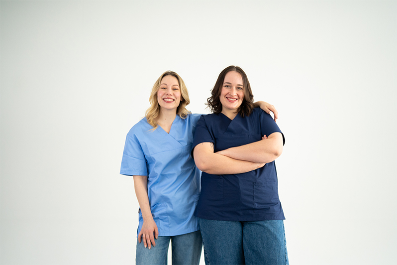 Zwei Kolleginnen in blauen Kasacks stehen lächelnd nebeneinander