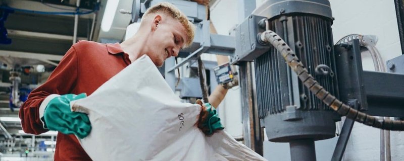 Mitarbeiter in roter Jacke und Schutzhandschuhen bedient Produktionsanlage