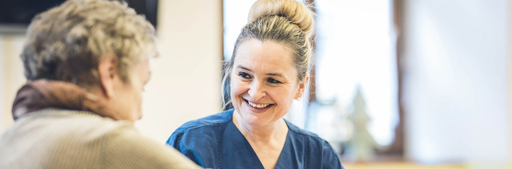 Pflegerin in blauer Uniform lächelt einen älteren Patienten an
