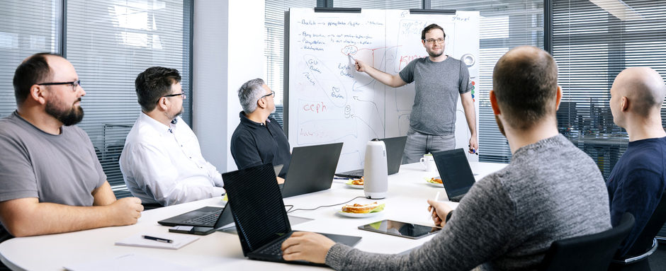 Team in Besprechung: Mann erklärt Konzept an Whiteboard vor mehreren Kollegen