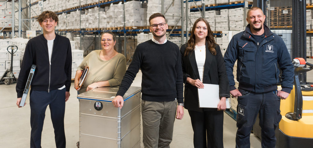 Fünf Mitarbeiter in einem Lager oder in der Produktion, alle lächeln in die Kamera