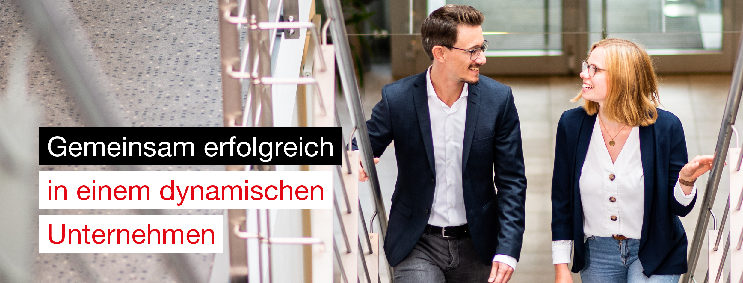 Junge, blonde Frau mit Brille und breitem Lächeln schaut direkt in die Kamera. Sie trägt einen dunkelblauen Blazer und steht in einem modernen Arbeitsumfeld. Links im Bild steht der Schriftzug 'Mach’s wie ich.'