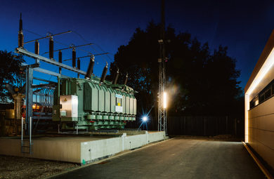 Hochspannungs-Transformator-Station bei Nacht mit grüner Ausrüstung und Strommasten