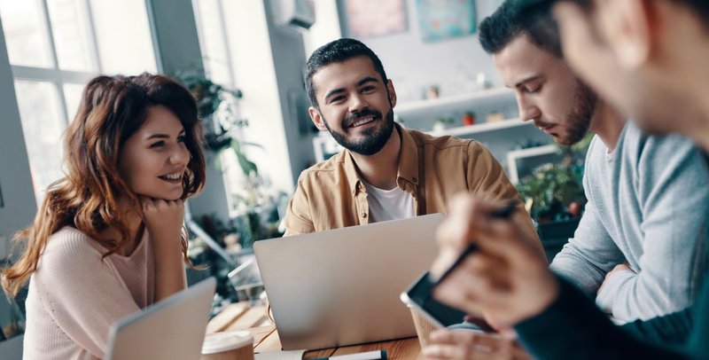 Team von vier Personen arbeitet zusammen an Laptop in modernem Büro mit Tageslicht