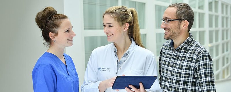 Drei Mitarbeitende im Gespräch über ein Tablet in einem hellen Klinikflur