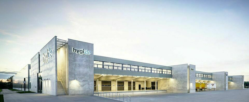 Firmengebäude der hygi.de mit Betonfassade, Logo am Eingangsbereich und Laderampen