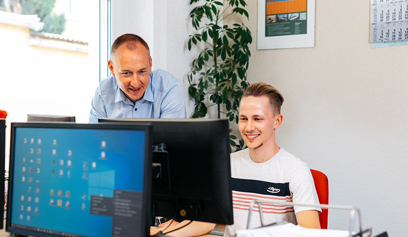 Zwei Kollegen arbeiten gemeinsam an einem Computerbildschirm in einer hellen Büroumgebung